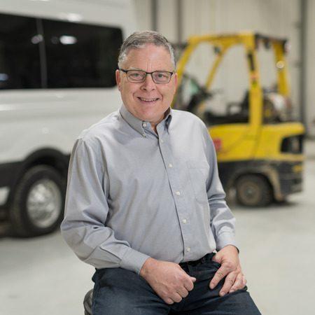 Man smiling for photo in a warehouse with a forklift in background