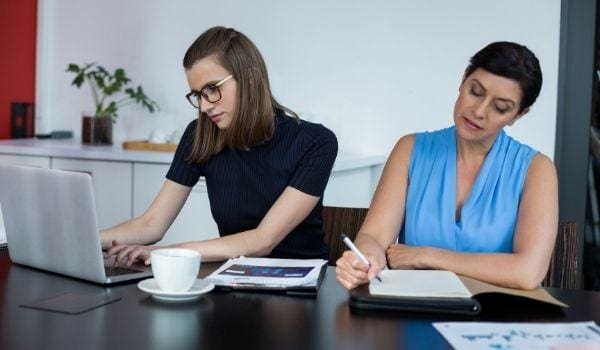 two ladies working at a table with computer and paper