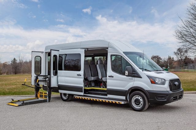 A side entry Ford Transit T6 wheelchair accessible van pictured in front of a field in summer.