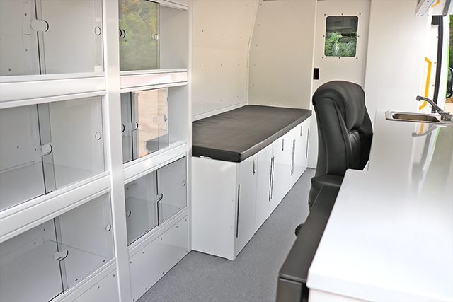 interior of mobile medical van with chair, desk, storage cabinets, patient bed and overhead cupboards for health counselling services