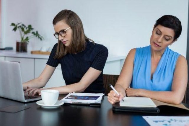 two ladies working at a table with computer and paper