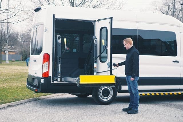 Man operating BraunAbility wheelchair lift on MoveMobility T6 Ford Transit side entry wheelchair van